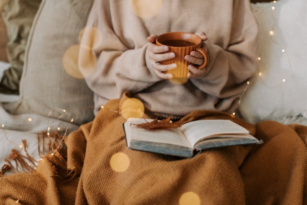 Persona bajo una manta con taza caliente y libro